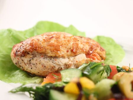 Close-up of chicken breast stuffed with mushrooms and cheese on lettuce, with a salad of fresh vegetables. Fresh pickles and tomatoes, chopped olives, cilantro and dill. Selective focusの写真素材
