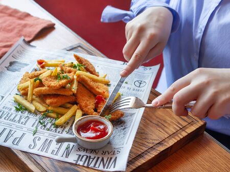 Deep-fried chicken breast. Garnished with french fries. Ketchup, chopped greens. The plate lies on a serving paperのeditorial素材