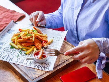 A girl in a blue blouse is using cutlery. Dine on deep-fried chicken breast with french fries....