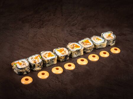 A serving of Japanese-style rolls arranged in a row against a dark background. Next to each slice is a drop of Japanese mayonnaise with soy sauceの写真素材