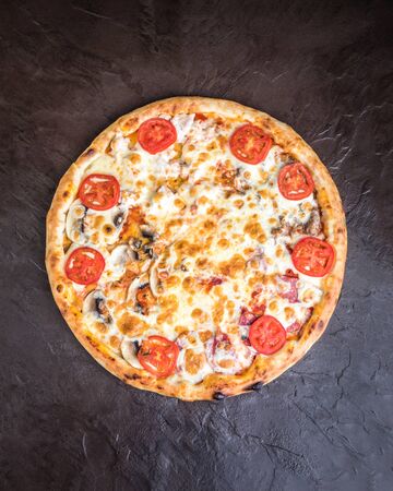 Pizza with mushrooms, tomatoes, smoked sausage and cheese on a dark background. Top view, close upの写真素材
