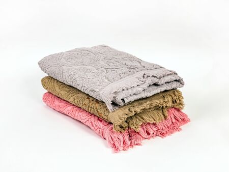 Three towels of different colors with a fringe are stacked in a stack on a light background. Gray, mustard, pink. Close-upの写真素材