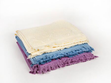 Three towels of different colors with a fringe are stacked in a stack on a light background, side view. Light yellow, blue, lavenderの写真素材
