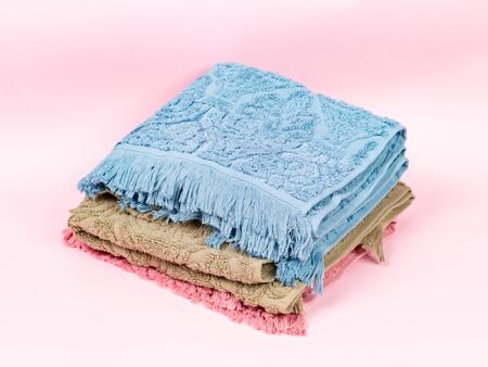 Three towels of different colors stacked in a stack on a pink background. Side view, close upの写真素材