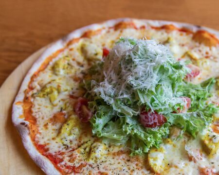 Pizza with chicken, tomatoes, fresh lettuce, sprinkled with grated parmesan. Fragment, close up. Selective focus, side viewの写真素材