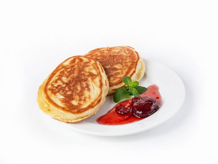 Two large pancakes on a plate with strawberry jam and mint leaves side view. Bistro menu, Russian breakfast. Close up on a white backgroundの写真素材