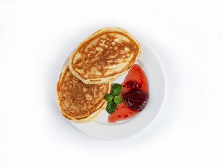 Two oval pancakes on a plate with strawberry jam, decorated with mint leaves, top view. Translucent jam, Russian breakfast. Close up on a white backgroundの写真素材