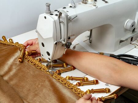 A girl sews a ribbon with decor to the edge of the curtain. Workspace of a seamstressの写真素材