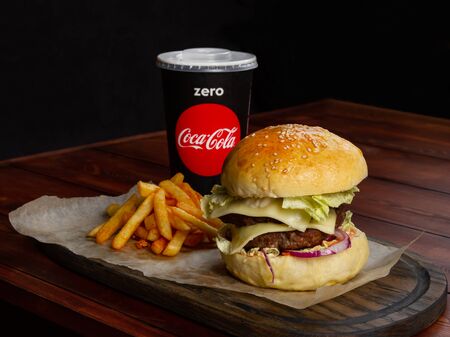 Burger with french fries and a paper glass with a drink on a cafe table. A table of boards, on a dark background. Serving paper and boardのeditorial素材