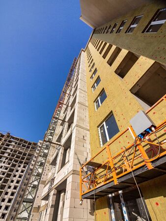 Various sections of the wall of the building under construction and an elevator for outdoor construction work. Walls covered and not covered with insulation material. Winter preparationsのeditorial素材