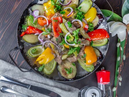 Juicy mixture of fried meat and vegetables in a pan. Bell pepper, zucchini, eggplant, onions, chopped greens. Cutlery, linen napkin. Salt, pepperの写真素材