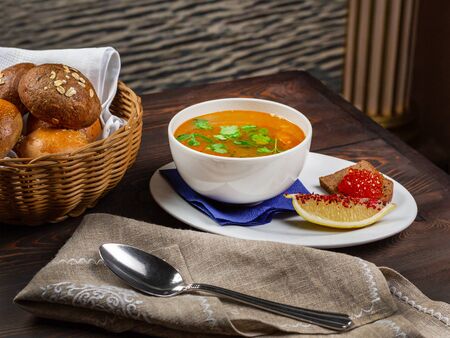 A plate of fish soup according to the Russian recipe on the served table of the restaurant. Cutlery. A slice of rye bread with red caviar. A slice of lemon sprinkled with spices. Basket with delicious bunsの写真素材