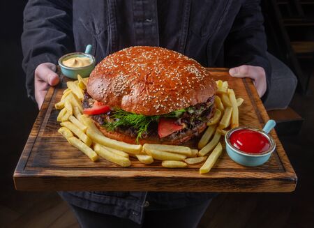 Huge burger on a serving plate with french fries and sauces. Close-up, selective focus. Jean jacketの写真素材