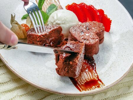 Dessert. Chocolate fondant is cut on a plate, close-up. Sliced strawberries, a scoop of ice cream. Garnished with physalis and mint leaves. Selective focusの写真素材