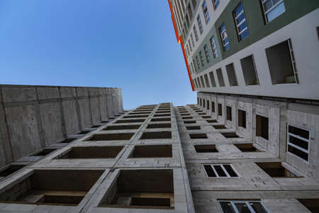 Completed multi-storey building near the building under construction, bottom view. Stages of...