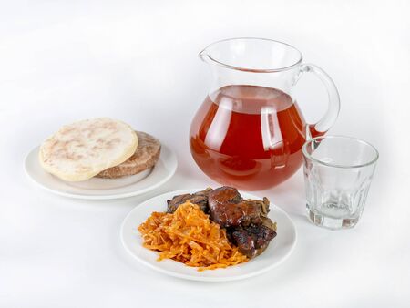 A serving of fried beef liver with stewed vegetables next to bread cakes and a glass jug of berry drink on a white backgroundの写真素材