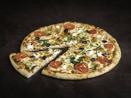 Big pizza on a dark background, side view. One serving is cut off and lies nearby. Sprinkled with fresh herbs. Selective focus, close-upの写真素材