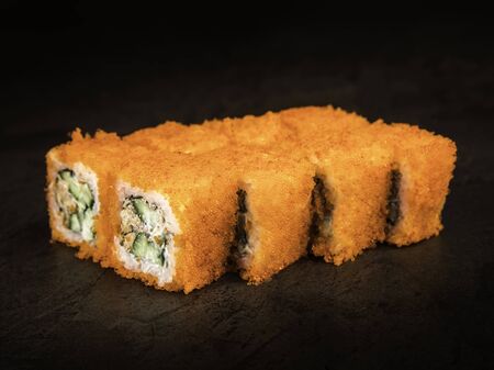 A portion of rolls of 8 pieces of flying fish covered with orange caviar. On a dark background, close up, selective focusの写真素材