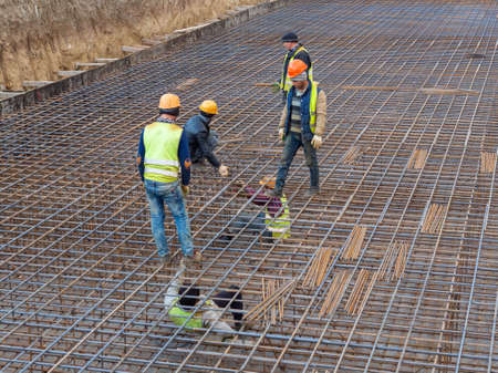 Several workers are preparing a frame of reinforcement for pouring the foundation of a high-rise...