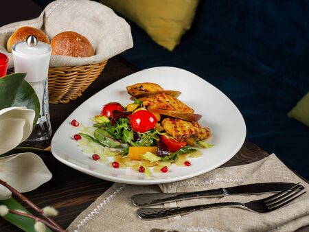 Beautifully decorated dish of fried chicken and a side dish on an original plate. Cutlery, salt, pepper. Linen cloth. Appetizing buns. Close up, selective focusの写真素材