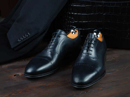 A pair of classic men's shoes on the surface of dark boards. Light wood pads. Selective focus. Jacket sleeve with buttons. Italian style. Side viewの写真素材