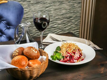 Vegetable salad on a restaurant table. Basket with delicious buns, linen napkin, cutlery. Transparent jug and glass with red wineの写真素材