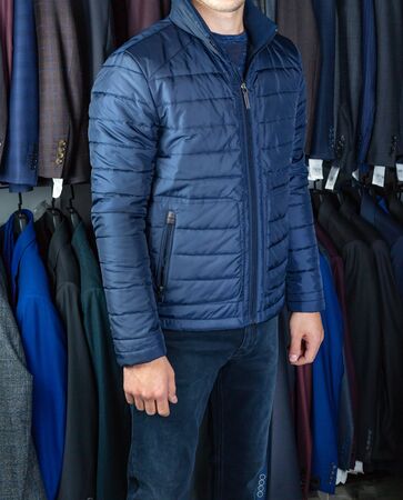 Young man in a short jacket poses on the background of shelves of clothes in the storeの写真素材