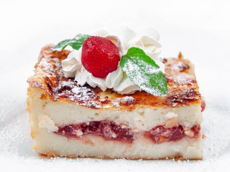 A piece of cake with fruit filling, decorated with strawberries, whipped cream and mint leaves on a white background. Close up, selective focus. Side viewの写真素材