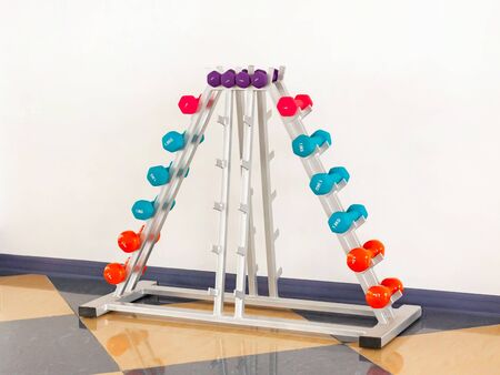 Multi-colored dumbbells of small weight are folded in a special rack against the wallの写真素材
