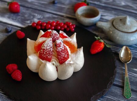 Meringue dessert on a serving board with fresh berries served for tea drinking. Against the background of abandoned boards. A teaspoon, a small teapot, a bowl. Foreground focusの写真素材