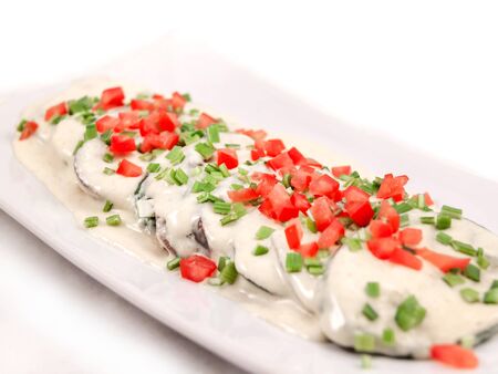 Sliced and fried eggplant is sprinkled with white sauce and sprinkled with chopped green onions and fresh tomatoes on a rectangular plate. Close up, selective focusの写真素材
