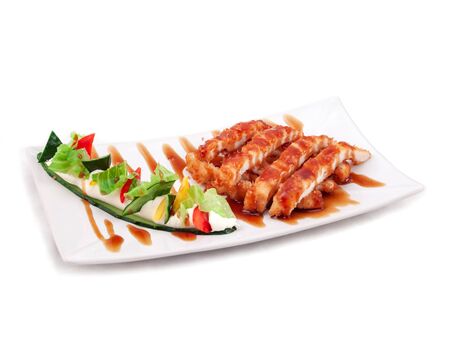 Appetizing slices of fried chicken breast are abundantly sprinkled with teriyaki sauce, on a rectangular plate. A dish of Japanese cuisine. Close up, selective focus. Isolateの写真素材