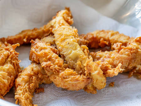 Large oblong pieces of breaded chicken are laid out on a napkin after frying to drain excess oil. Side view, close-up. Selective focusの写真素材