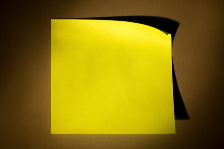 Blank yellow adhesive post-it note stuck on stainless steel surface of refrigerator in warm yellow...
