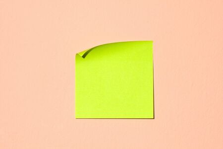 Blank green-yellow adhesive post-it note stuck on a pink wall.の写真素材