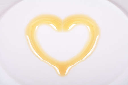 Yellow honey in the shape of heart on a white plate.の写真素材