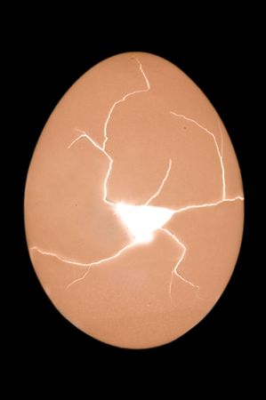 Cracking egg with hole and radiant light from inside on black
