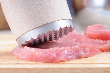 Tenderization of fresh pork steaks on wooden chopping board.