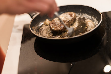the process of cooking beef steak in a frying pan with butter and rosemaryの写真素材