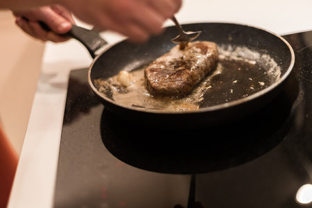 the process of cooking beef steak in a frying pan with butter and rosemaryの写真素材