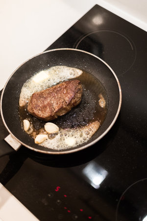 the process of cooking beef steak in a frying pan with butter and rosemaryの写真素材