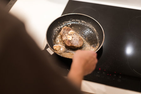 the process of cooking beef steak in a frying pan with butter and rosemaryの写真素材