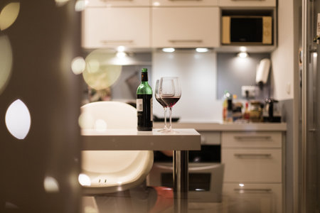 Two glasses of wine and a bottle on the table against the background of a person preparing dinner in a cozy atmosphereの写真素材