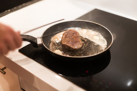 the process of cooking beef steak in a frying pan with butter and rosemaryの写真素材