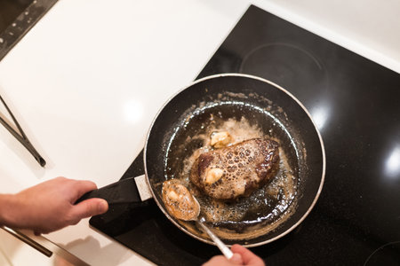 the process of cooking beef steak in a frying pan with butter and rosemaryの写真素材