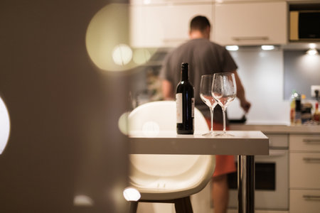 Two glasses of wine and a bottle on the table against the background of a man preparing dinner in a cozy atmosphereの写真素材