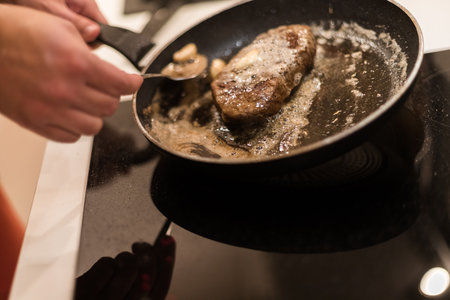 the process of cooking beef steak in a frying pan with butter and rosemaryの写真素材