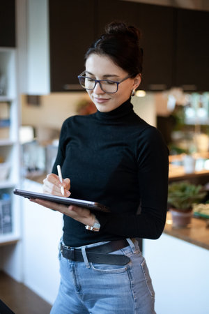woman in glasses taking notes on tablet She is focused, wearing a black turtleneck