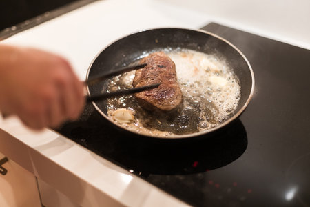 the process of cooking beef steak in a frying pan with butter and rosemaryの写真素材