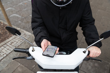courier on a courier on a scooter looks at the map on his phone and looks for an address to deliver an orderの写真素材